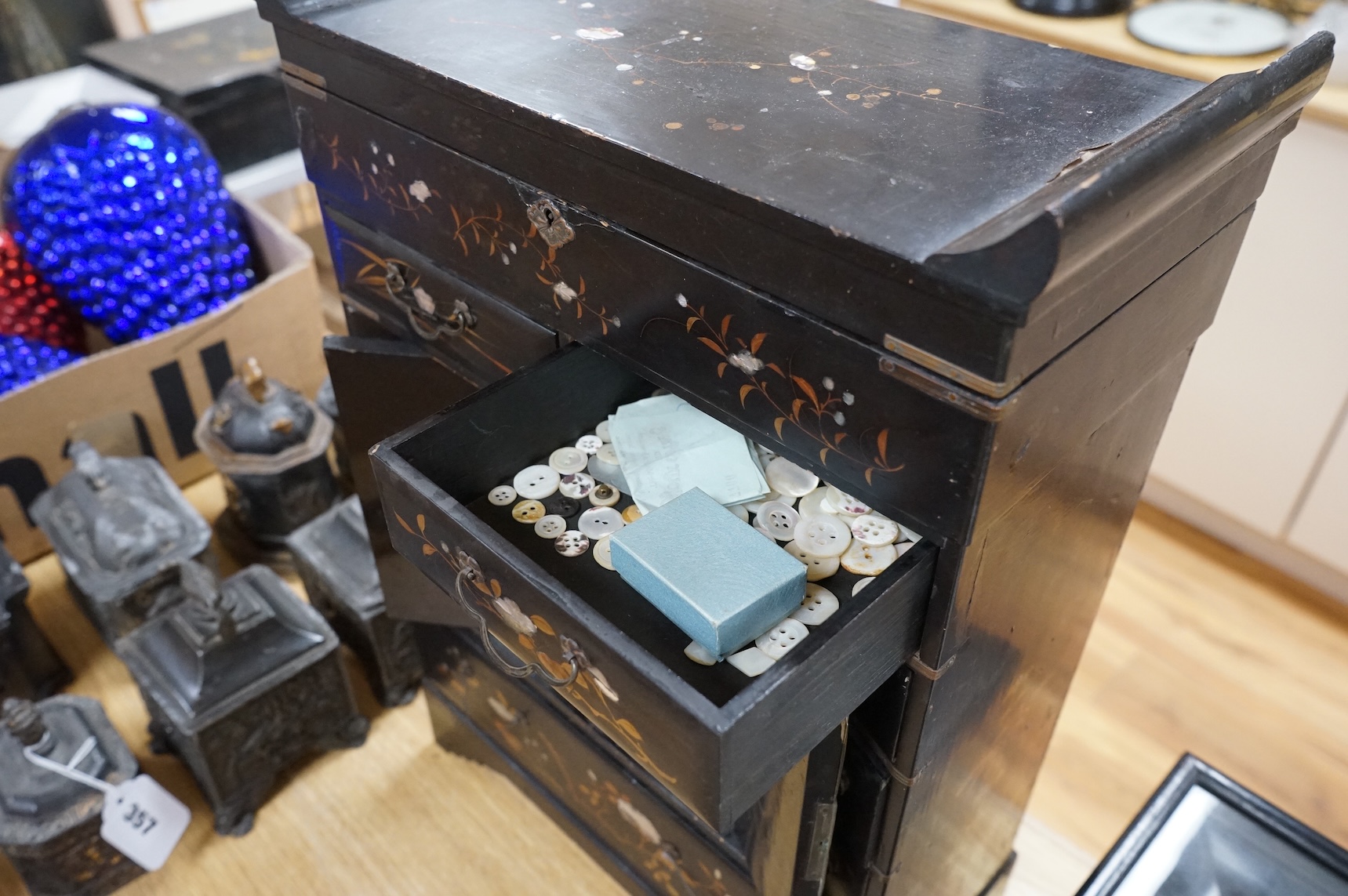 A Japanese lacquer table cabinet with inset porcelain panels, the drawers filled with sundry objects, clay pipes, decanter stoppers, etc, together with a black japanned wall clock, the dial inscribed F. L Hausburg, Paris